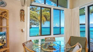 A room with a glass table surrounded by wicker chairs, large windows with a view of the sea, and a bamboo wall decor. - *NEW* Turtle-Watching Oceanfront Lanai in West Maui (Lahaina)