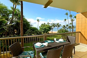 A balcony with wicker furniture, a table set for two, and a view of the beach and palm trees. - New Fall Sale Keawakapu Beach Condo with Private Laundry (Kihei)