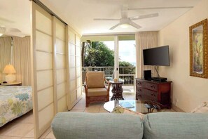 A hotel room with a bed, a sofa, a television, a small table, and a balcony with a chair. - New Fall Sale Keawakapu Beach Condo with Private Laundry (Kihei)