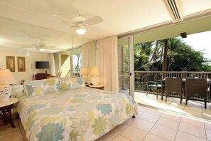 A hotel room with a balcony, a bed with floral bedding, a ceiling fan, and a TV. - New Fall Sale Keawakapu Beach Condo with Private Laundry (Kihei)