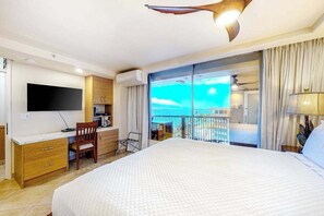 Quarto de hotel com cama, secretária com televisão de tela plana, uma cadeira, varanda com vista para o mar e luminária no teto.