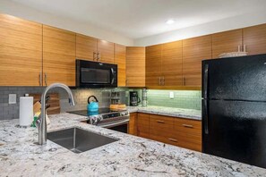 A kitchen with wooden cabinets, a black microwave, a black refrigerator, a sink, and a stove. - *NEW* Garden-Lanai Kihei Condo Near Kamaole Beach III (Kihei)