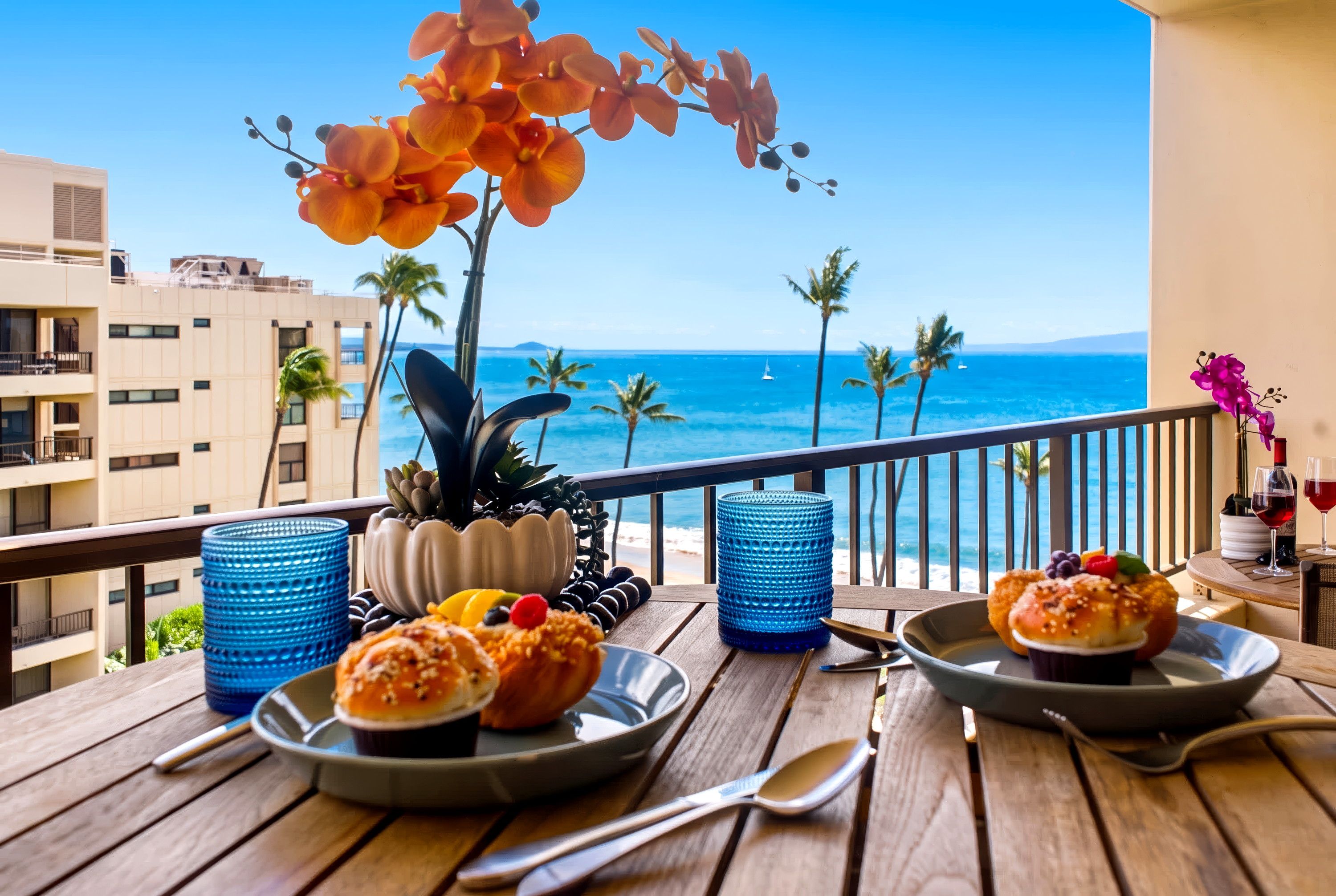 A balcony with a view of the ocean, a table with plates of food, and decorative plants.