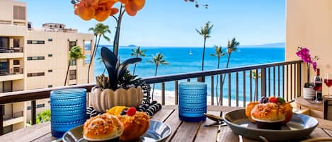 A balcony with a view of the ocean, a table with plates of food, and decorative plants.
