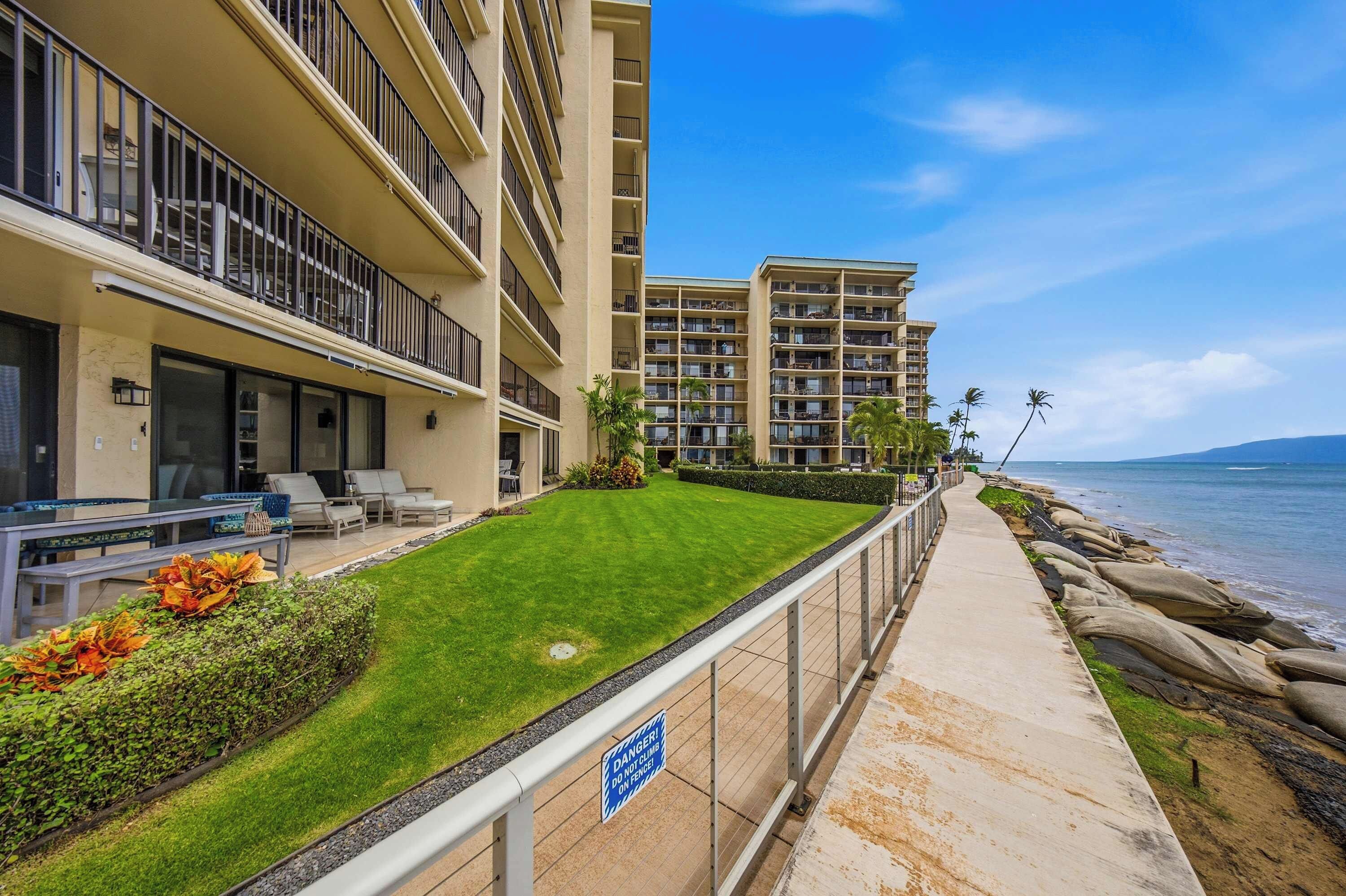 A beachfront hotel with multiple balconies, a well-maintained lawn, and a clear view of the ocean.