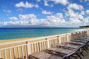 Blick auf einen Strand mit einer Holzterrasse, Liegestühlen und einem klaren, blauen Meer.