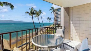 A balcony with a glass table, chairs, and a view of the beach and ocean. - NEW Fall $ale Third-Floor Kahana Sunsets and Ocean Views Near Ka'anapali (Lahaina)