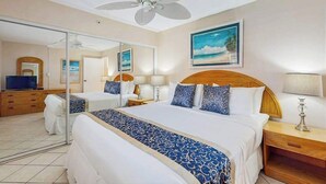 A hotel room with a large bed, a ceiling fan, a TV, and a painting of a beach. - NEW Fall $ale Third-Floor Kahana Sunsets and Ocean Views Near Ka'anapali (Lahaina)