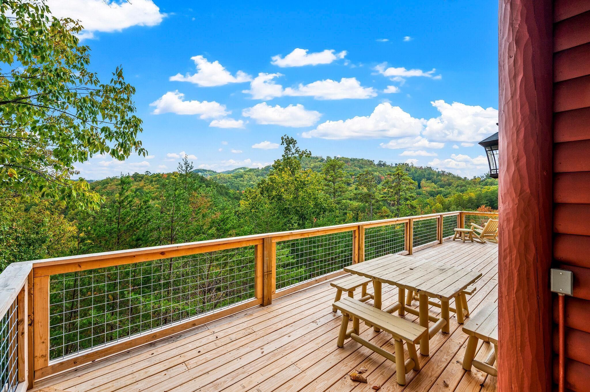 A wooden deck with a picnic table and chairs, overlooking a forested hillside.