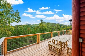 Eine Holzterrasse mit Picknicktisch und -stühlen, mit Blick auf einen bewaldeten Hügel.