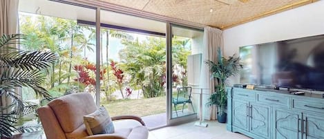 A modern living room with a sofa, a television, and a glass door leading to a garden.