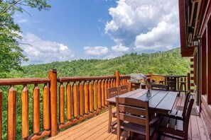 Um deck de madeira com mesa e cadeiras, com vista para uma encosta arborizada.