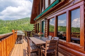 Um deck de madeira com mesa e cadeiras, com vista para um morro arborizado.