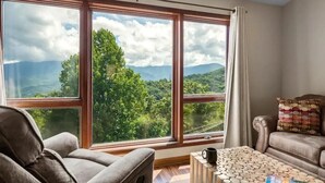 A room with a large window offering a mountain view, a sofa, and a coffee table. - Reed's Retreat (Gatlinburg)