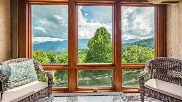 A room with a large window, wicker furniture, and a view of a forest and mountains. - Reed's Retreat (Gatlinburg)