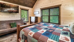 Una camera accogliente con travi in legno, un letto grande con una coperta colorata, un divano con un cuscino verde e un quadro raffigurante un ruscello.