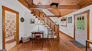 Interior de madeira com escada, uma mesa com abajur e uma porta com janela.