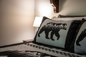 Ein Bett mit gemusterten Betttextilien und einem Kopfkissen mit Bärenmotiv.
