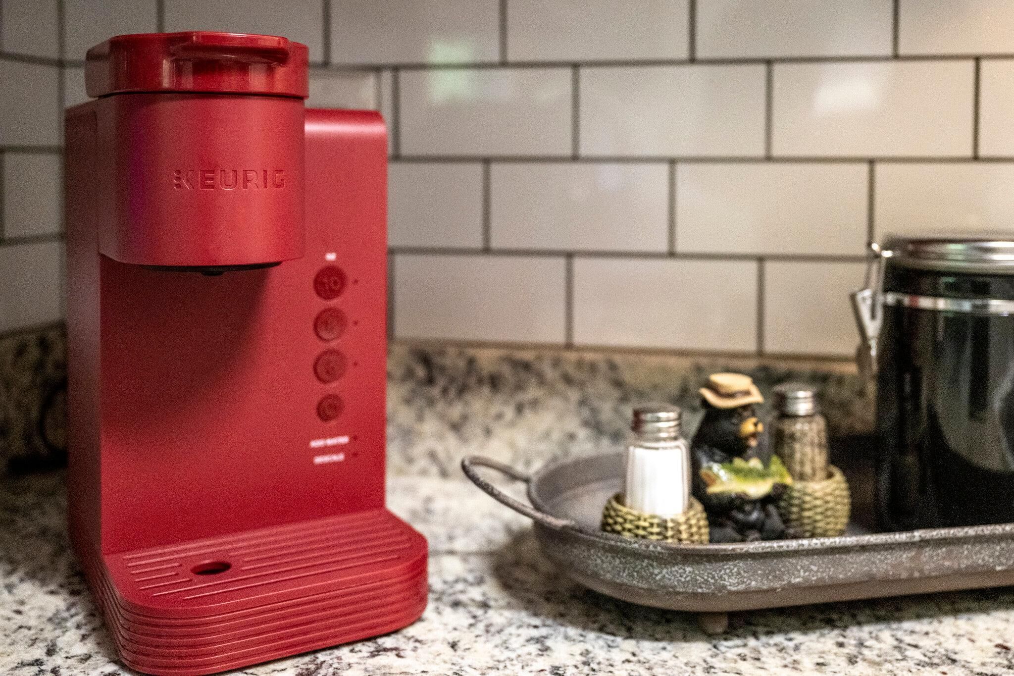 A red Keurig coffee maker on a kitchen counter with a tray of salt and pepper shakers and a black coffee pot.