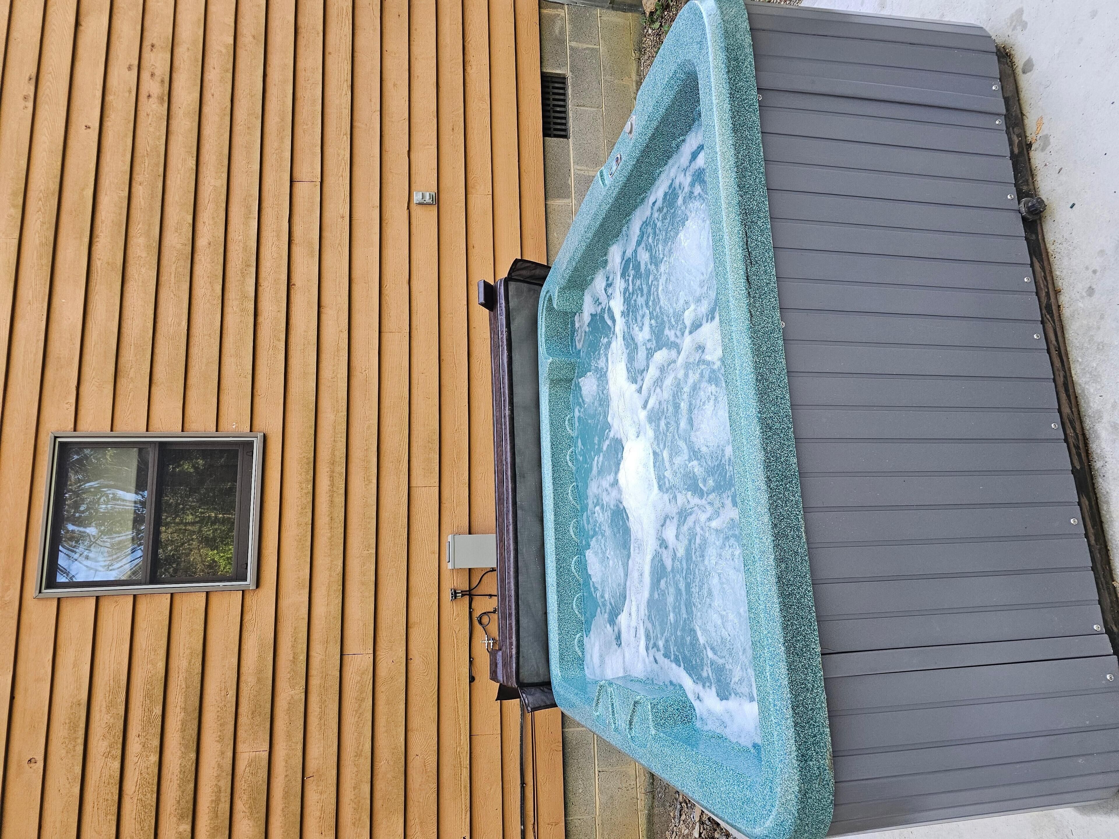 A wooden deck with a hot tub, a window, and a grey roof.