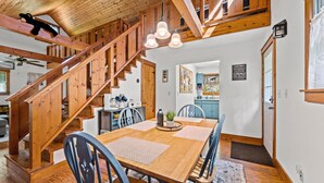 Uma escada de madeira leva a uma sala de jantar com mesa e cadeiras.