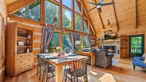 A spacious wooden cabin interior with a dining area, fireplace, and large windows. - Second Fiddle (Sevierville)