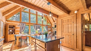 A wooden cabin interior with a dining area, kitchen, and large windows. - Second Fiddle (Sevierville)