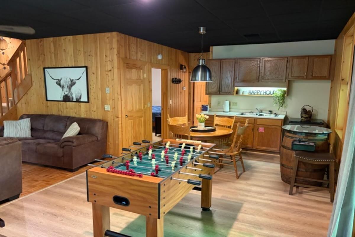 Ein gemütliches Zimmer mit Fußballtisch, einer Couch, Holzwänden, einer Küchenzeile und einem Esstisch.