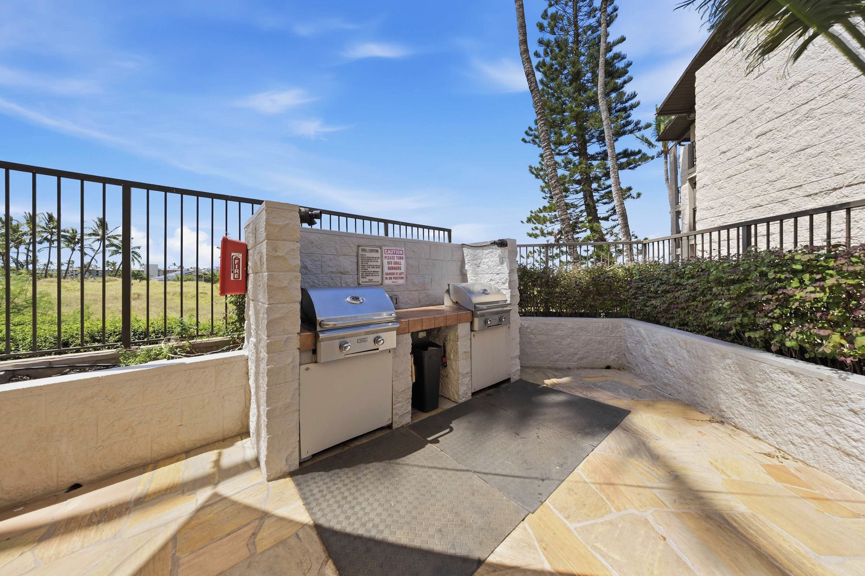 An outdoor grill area with a fire extinguisher, caution signs, and a stone wall.