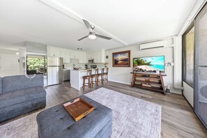 A modern living space with a grey sofa, a wooden ottoman, a kitchen area, and a dining set. - *New* Fall $pecial Ocean-View Kihei Escape Across from the Beach (Kihei)