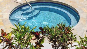 Ein kreisrunder Pool mit Mosaikbordüre, umgeben von Steinplatten und Pflanzen.