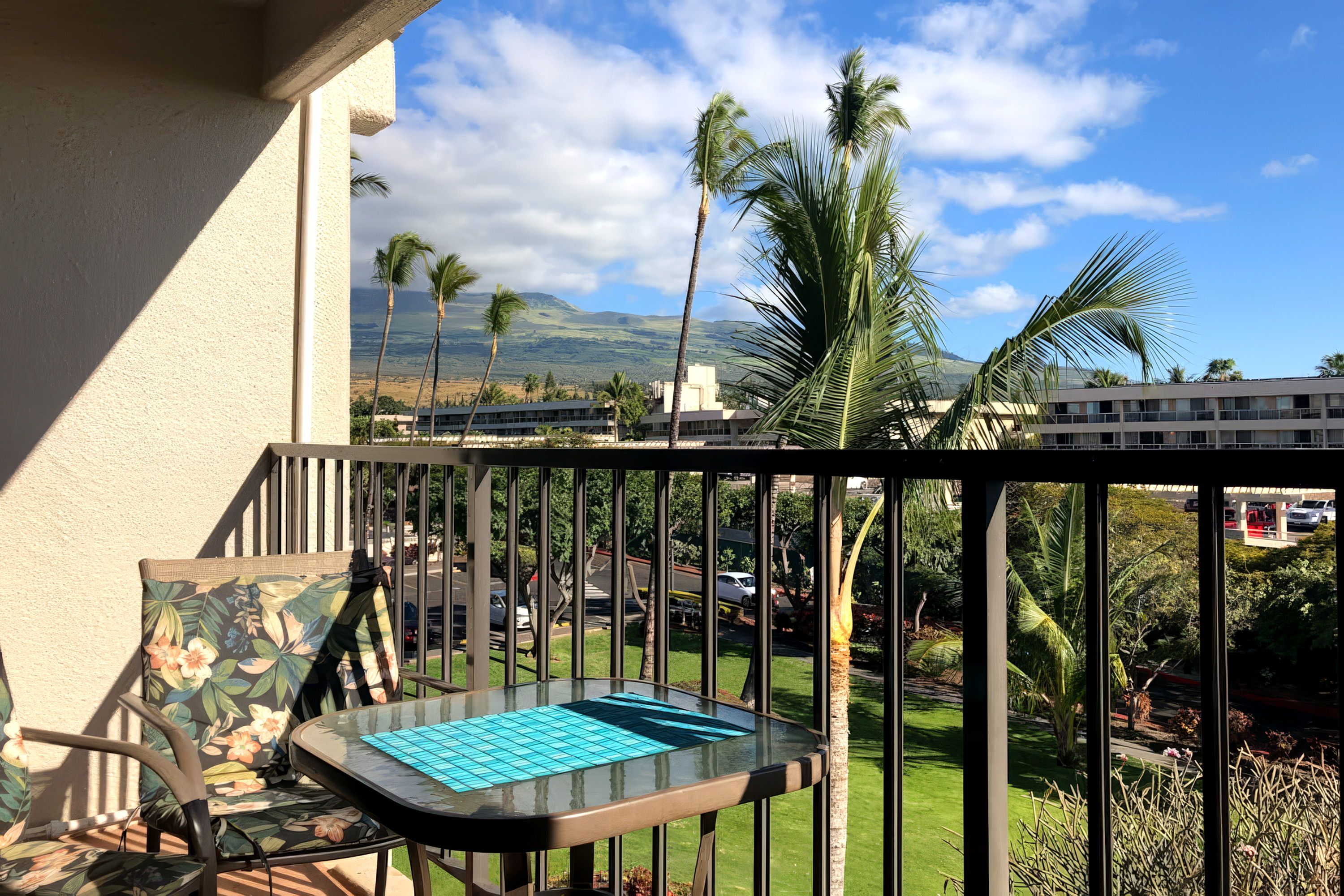 A balcony with a glass table and chairs, overlooking a view of palm trees and a distant mountain range.