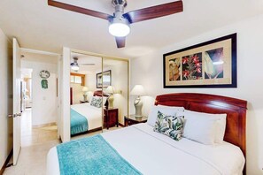 A hotel room with a bed, a ceiling fan, a mirror, a framed picture on the wall, and a door leading to another room. - NEW Oceanfront Kahana Retreat With Heated Pool and Lanai (Lahaina)