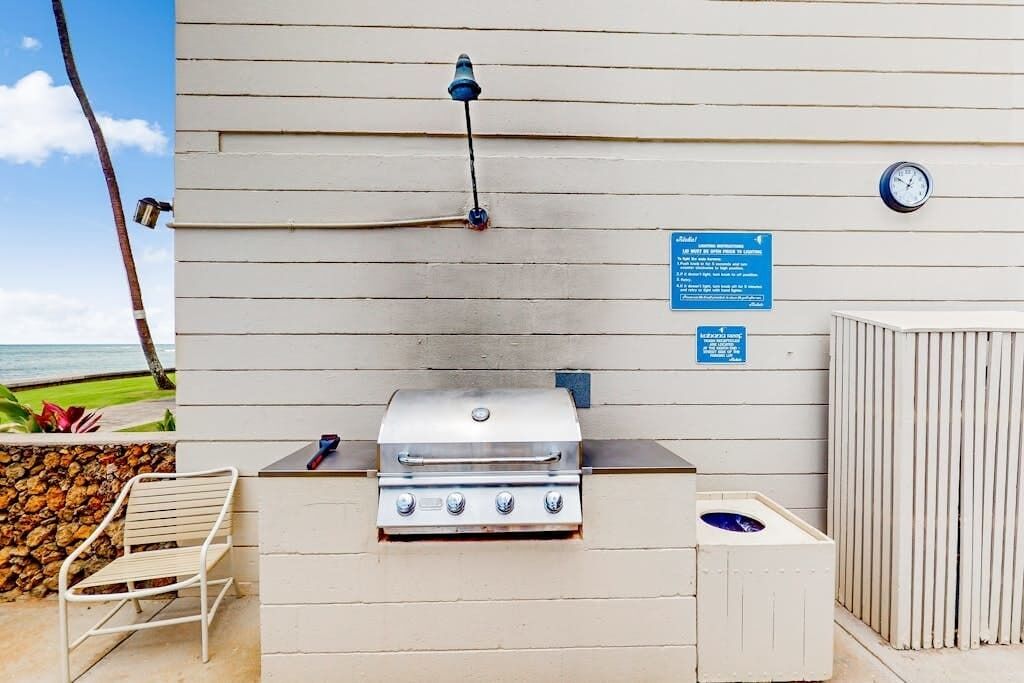 Un espace barbecue extérieur avec un mur en pierre, une chaise en métal et une horloge fixée au mur.