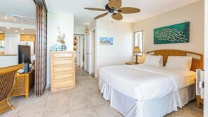 A hotel room with a bed, a desk, a chair, a dresser, a ceiling fan, and artwork on the walls. - NEW Fall Sale Fifth Floor Kahana Oceanfront with Two Lanais (Lahaina)