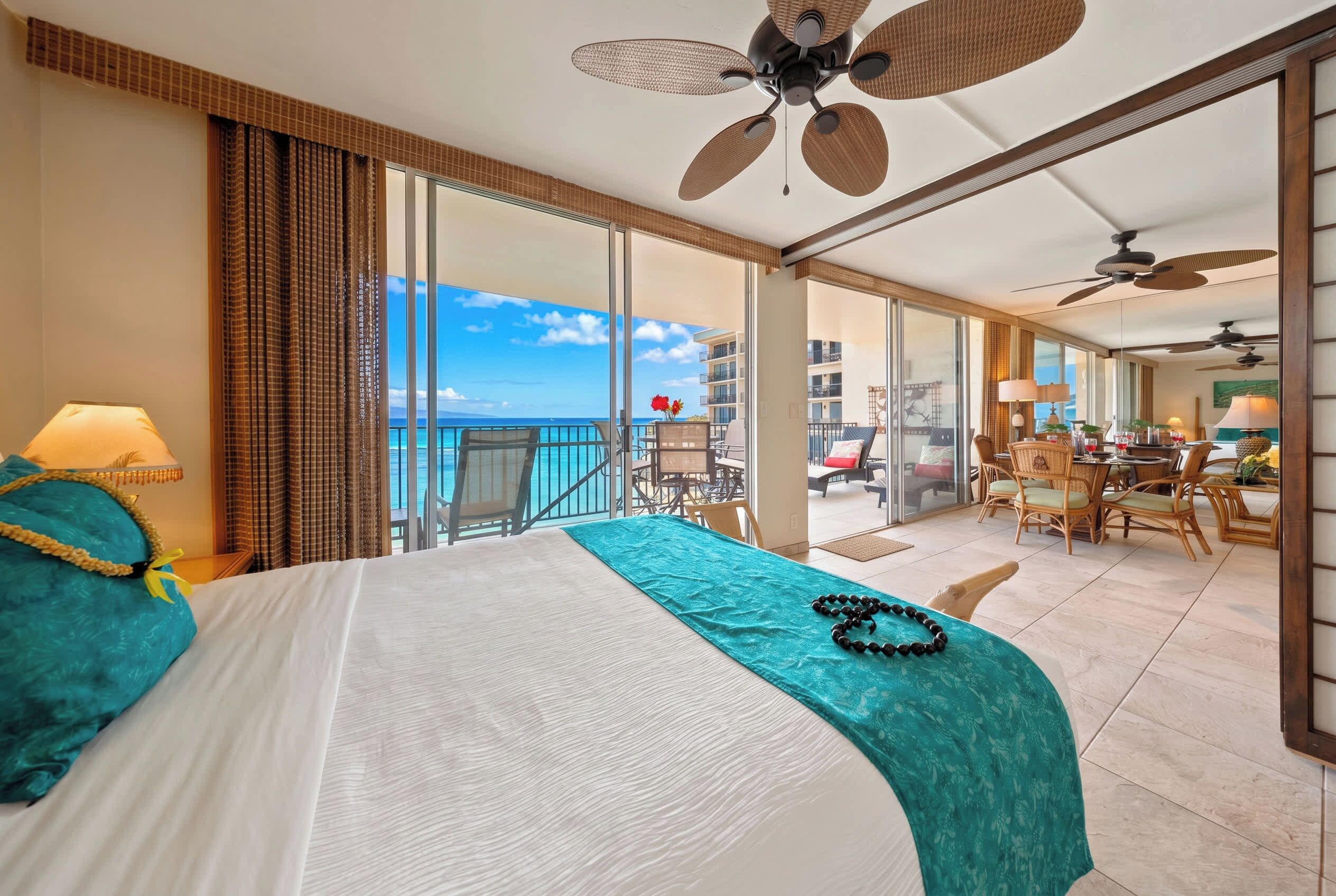 A hotel room with a balcony, a bed with a teal bedspread, and a view of the ocean.
