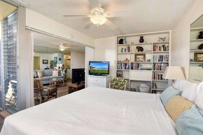Ein Schlafzimmer mit einem großen Bett, einem Fernseher, einem Bücherregal und einer Glastür, die auf einen Balkon führt.