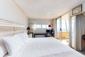 Habitación de hotel con una cama grande, un escritorio con computadora, una silla y un balcón con vistas.