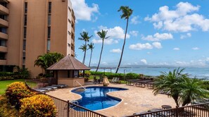 A hotel pool area with a view of the ocean, palm trees, and a building in the background. - NEW Fall Deal Roomy Maalaea Bay Condo for a Family Beach Week (Wailuku)