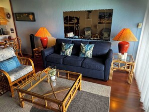 A living room with a dark blue sofa, two wooden side tables with lamps, a glass coffee table, and wicker chairs. - *NEW* Room for Eight Near Kamaole III, Pet-Friendly Kihei Condo (Kihei)