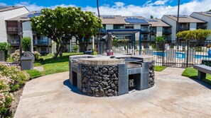 A courtyard with a stone fire pit, a pool, and a building with solar panels. - *NEW* Room for Eight Near Kamaole III, Pet-Friendly Kihei Condo (Kihei)