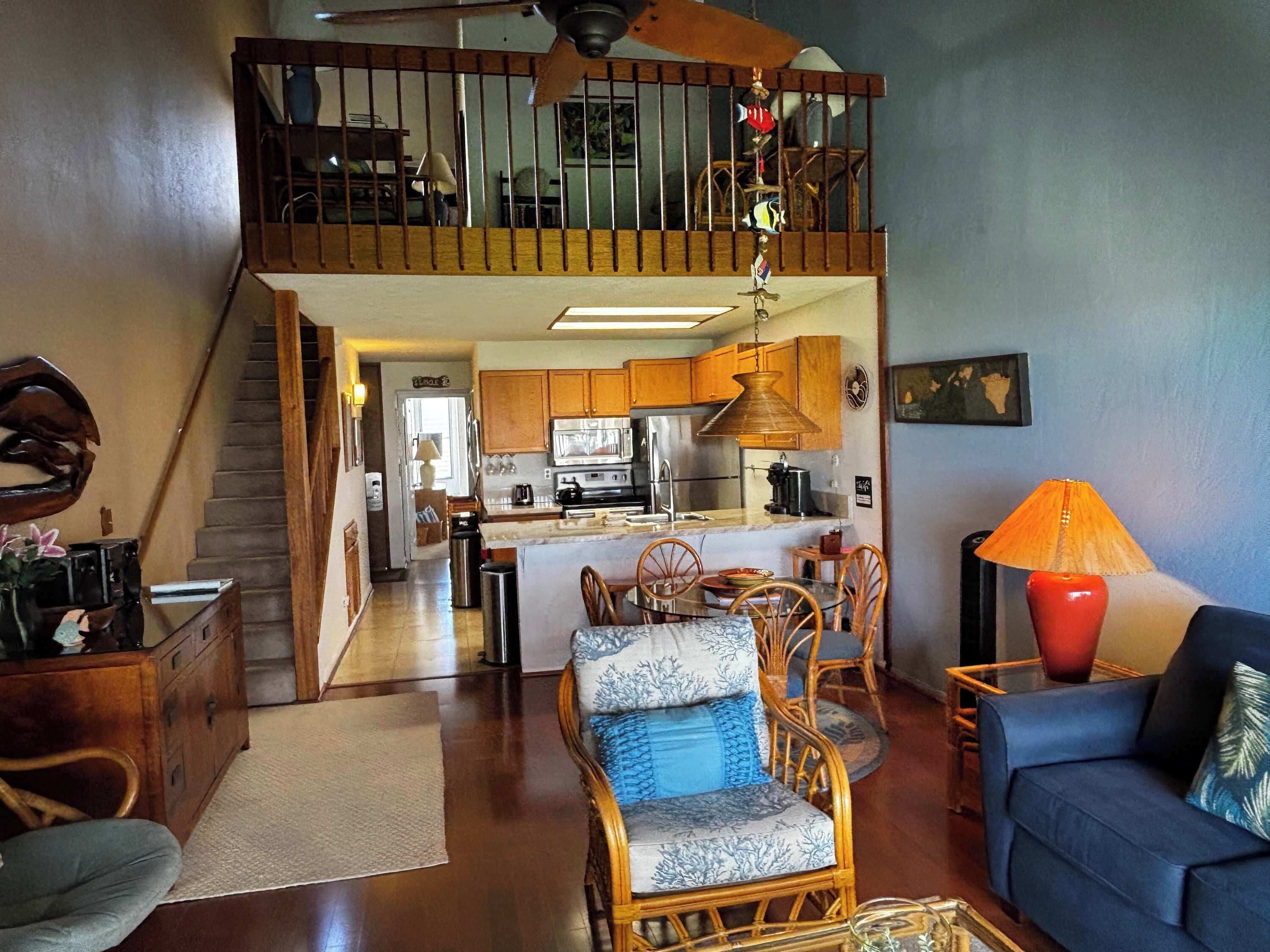 A spacious living area with a high ceiling, a kitchen with modern appliances, and a dining area with wicker furniture.