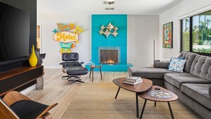 A modern living room with a fireplace, a sofa, a coffee table, and a TV. - The Martini Lounge | Mid-Century with Private Pool (Palm Springs)