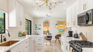 A modern kitchen with white cabinetry, a central island, a stove, and a dining area with chairs. - The Martini Lounge | Mid-Century with Private Pool (Palm Springs)