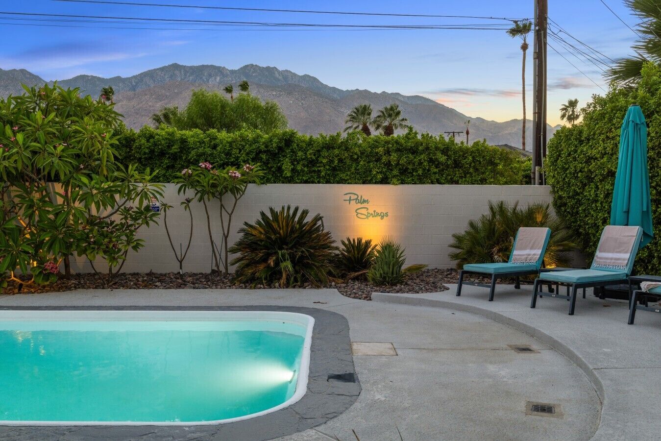 Ein Swimmingpool mit Bergblick, eine Wand mit der Aufschrift 'Palm Springs' und Liegestühle.