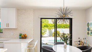 A modern kitchen with white cabinets, a patterned backsplash, and a dining area with a round table and chairs. - The Martini Lounge | Mid-Century with Private Pool (Palm Springs)