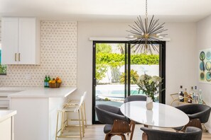 Eine moderne Küche mit weißen Schränken, einer gemusterten Spritzschutzleiste und einem Essbereich mit rundem Tisch und Stühlen.
