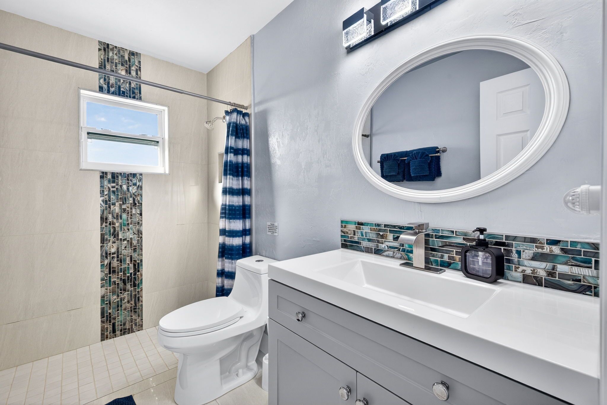 A bathroom with a toilet, a shower, a sink with a mirror, and a window.