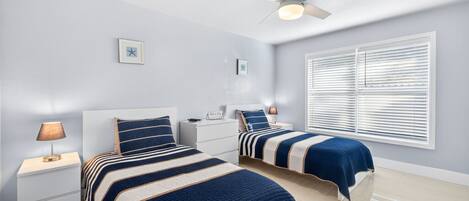 A bedroom with two beds, a ceiling fan, and a window with blinds.