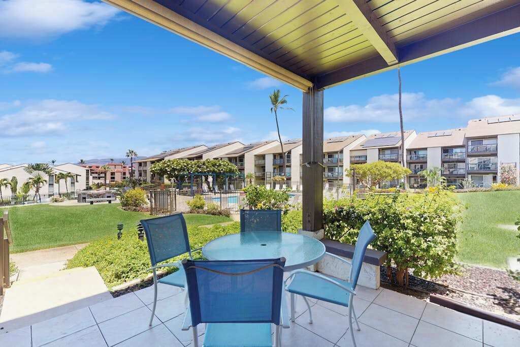 Une terrasse extérieure couverte, dotée d’une table et de chaises en verre, entourée de verdure et offrant une vue sur des immeubles résidentiels.
